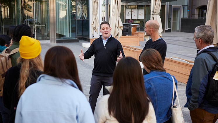 A group of students listening to a lecture presentation outdoors